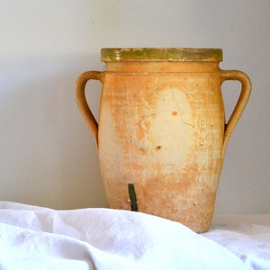 May include: A large, terracotta-colored ceramic jar with two handles and a lid. The jar has a rustic, aged appearance with a green glaze on the bottom.