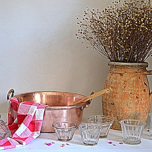 May include: A copper pot with a wooden spoon, a terracotta jar with dried flowers, and a collection of clear glass cups on a white surface.