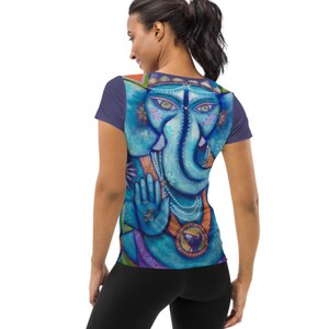 May include: A blue and purple t-shirt with a colorful illustration of the Hindu deity Ganesha on the back. The illustration features a blue elephant head with a third eye, a beaded necklace, and a hand gesture.
