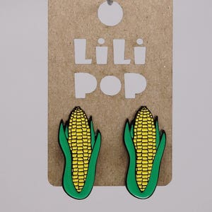 Peut inclure: Une paire de boucles d'oreilles en forme d'épi de maïs sur une carte marron avec le texte "Lili Pop" en lettres blanches.