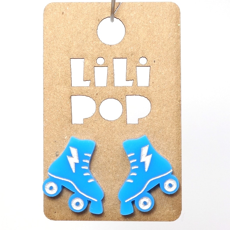 May include: A pair of blue roller skate earrings with white lightning bolts and wheels. The earrings are on a brown card with the text "Lili Pop" cut out.
