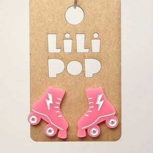 May include: Pink roller skate earrings with a silver lightning bolt design. The earrings are on a brown card with the text "Lili Pop" in white.