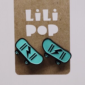 May include: A pair of teal blue skateboard earrings with black lightning bolt designs. The earrings are on a brown card with the text "Lili Pop" printed in white.