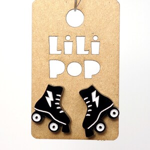 May include: A pair of black roller skate earrings with white lightning bolt designs. The earrings are displayed on a brown card with the text "Lili Pop" cut out.