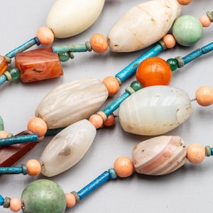 Può includere: Una collana multifilo con perline di vari colori, tra cui bianco, arancione, verde e rosso. Le perline sono realizzate in agata, cornalina e altri materiali naturali.