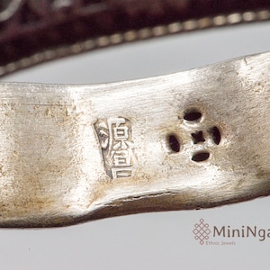 May include: Close-up of a silver ring with a Chinese character inscription and four small holes. The inscription reads "寶貴".
