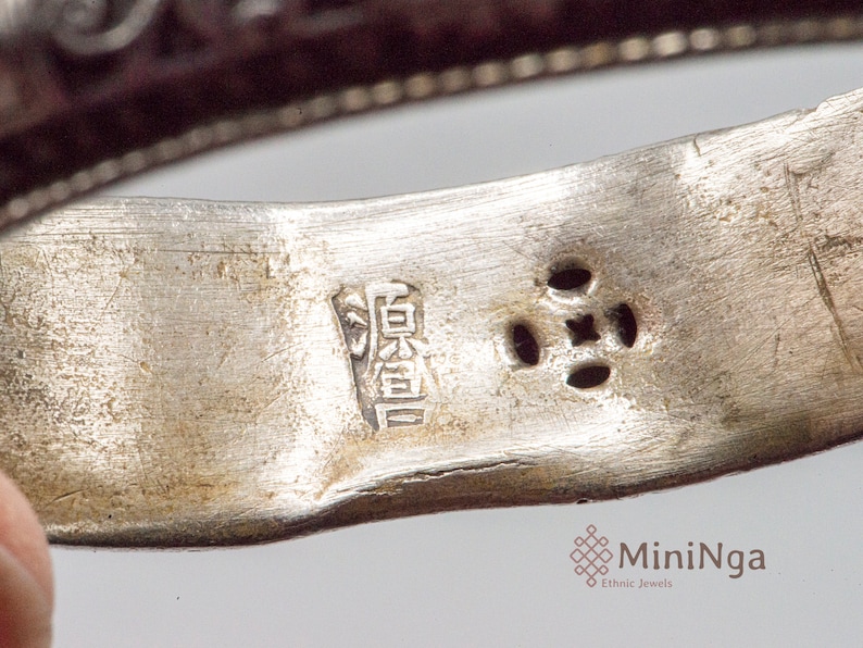 May include: Close-up of a silver ring with a Chinese character inscription and four small holes. The inscription reads "寶貴".