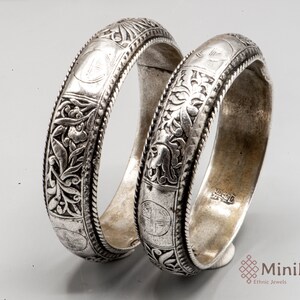 May include: Two silver bracelets with intricate floral and geometric designs. The bracelets are made of silver and have a polished finish.