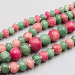 May include: Close-up of three strands of beaded necklaces. The beads are a mix of pink, green, and silver. The beads are round, oval, and disc-shaped. The necklaces are displayed on a gray background.