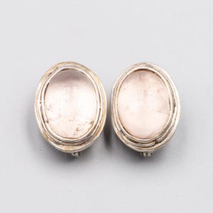 May include: Two oval earrings with a silver metal setting. Each earring features a pale pink, possibly rose quartz, stone. The design is simple and elegant, suitable for everyday wear or special occasions.