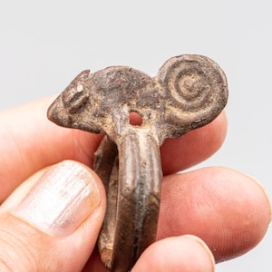 Puede incluir: Una taza de cerámica blanca con asa negra y el texto "But First, Coffee" en negrita negra. La taza se encuentra sobre un fondo borroso, sugiriendo un ambiente acogedor.