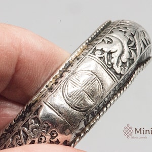 May include: Silver bracelet with intricate floral and geometric designs. The bracelet has a rope-like border and a central motif of a cross within a circle.
