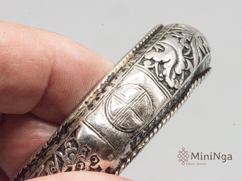 May include: Silver bracelet with intricate floral and geometric designs. The bracelet has a rope-like border and a central motif of a cross within a circle.