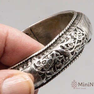 May include: Silver bracelet with intricate floral designs and a beaded edge.