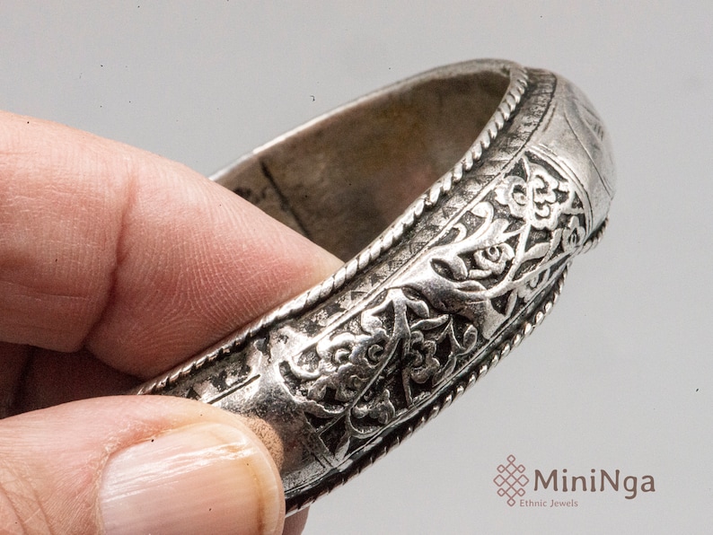 May include: Silver bracelet with intricate floral designs and a beaded edge.