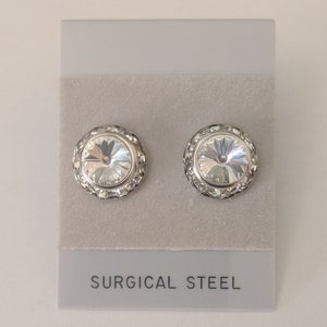 May include: A pair of silver stud earrings with clear crystal stones. The earrings are on a white card with the words "SURGICAL STEEL" printed on it.