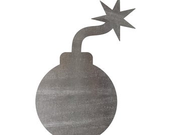 May include: A flat, circular grey wooden cutout shaped like a cartoon bomb. The object features a curved fuse extending from the top, ending in a pointed, star-shaped spark. The surface displays a visible wood grain texture throughout the entire piece.