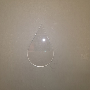 May include: A clear plastic teardrop shape cutout on a gray background.