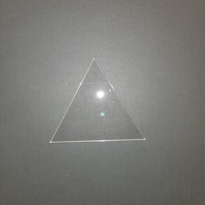 May include: A clear glass triangle, possibly a prism, on a gray background.