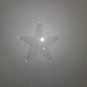May include: A clear plastic star-shaped cutout on a gray background.