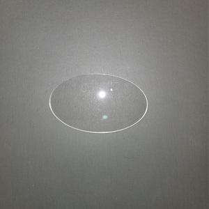 May include: A clear, round, glass watch crystal.