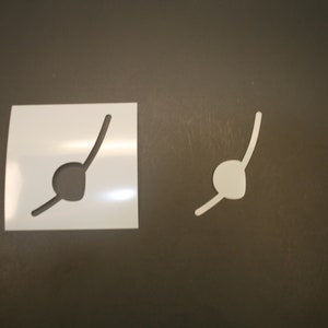 May include: Two white stencils, one on a white background and one on a brown background, both with a curved line and a circle at the end of the line.