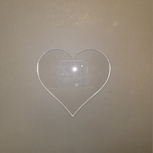 May include: A clear plastic heart-shaped cutout on a brown background.