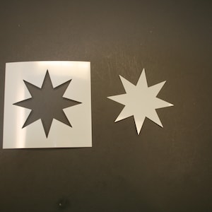 May include: Two white star-shaped stencils, one larger than the other, are placed on a brown surface.