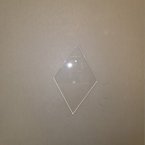 May include: A clear diamond-shaped piece of glass on a gray background.