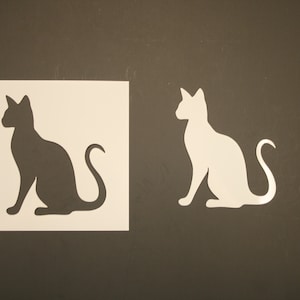 May include: A stencil with two cat silhouettes, one black and one white, on a brown background.