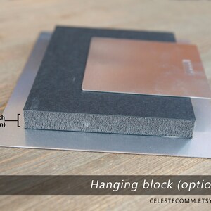 May include: A close-up of a metal print with a hanging block attached to the back. The hanging block is 3/4 inch (19 mm) thick. The metal print is on a wooden surface.