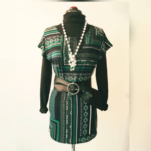 May include: A green and black patterned dress with a black belt and a white pearl necklace. The dress has a geometric design.