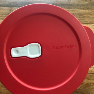 May include: Red plastic Tupperware container lid with a white latch and the word "Tupperware" printed on the lid.