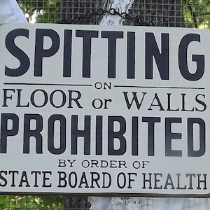 May include: A rectangular wooden sign with the words "SPITTING ON FLOOR or WALLS PROHIBITED" in black lettering. The sign also includes the text "BY ORDER OF STATE BOARD OF HEALTH."