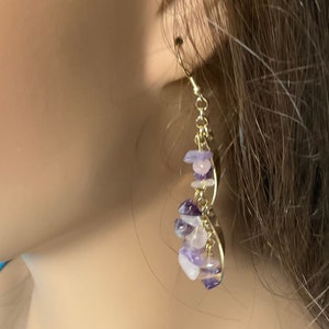 May include: Gold-toned earrings with a cascading design. Each earring features a series of small, irregularly shaped amethyst and rose quartz stones. The stones are strung together with gold-colored wire, creating a delicate and elegant accessory.