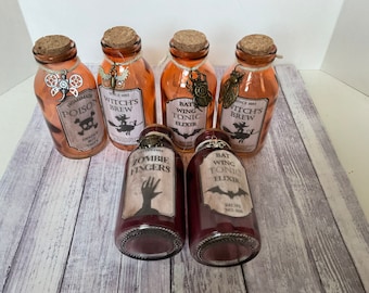 May include: Six small glass bottles with cork stoppers and labels. The labels have Halloween-themed text and images, such as "Witch's Brew", "Zombie Fingers", and "Bat Wing Tonic Elixir".