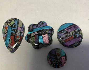 May include: Four colorful resin cabochons with a geometric pattern in shades of blue, purple, pink, and green. The cabochons are set against a white background.