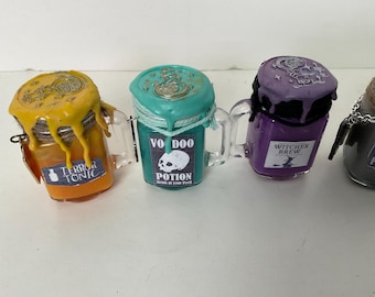 May include: Four small glass jars with lids, each filled with a different colored liquid and decorated with Halloween-themed labels. The labels read "Terror Tonic", "Voodoo Potion", "Witches Brew", and "Anti-Potion".