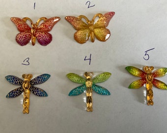 May include: Five decorative metal butterflies and dragonflies with gold accents. The butterflies are in shades of red, yellow, and orange. The dragonflies are in shades of blue, green, and red.