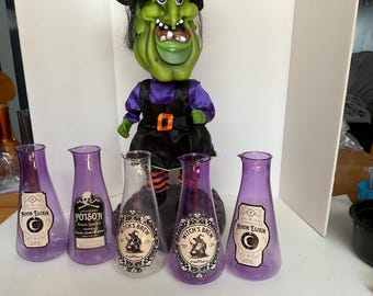 May include: Five purple glass bottles with different Halloween-themed labels. The labels include "Moon Elixir", "Poison", "Witch's Brew", and "Witch's Brew".