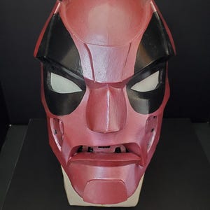 Pu&ograve; includere: Una maschera rossa e nera con aperture bianche per gli occhi. La maschera ha un'espressione severa ed &egrave; probabilmente un costume o un accessorio. La maschera &egrave; realizzata in un materiale solido e ha una finitura liscia.