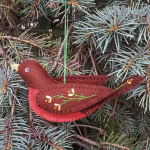 May include: A felt Christmas ornament shaped like a red robin with a brown body and a green stem with yellow flowers embroidered on it.