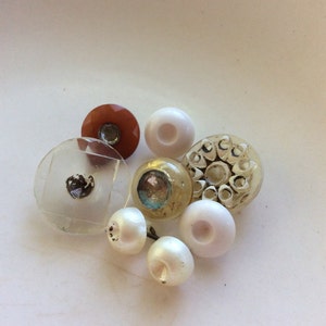 May include: Assortment of vintage buttons in various colors and styles, including clear, white, brown, and blue. Some buttons have a raised design.