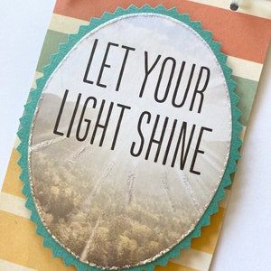 May include: A teal blue circle with a white background and the text "Let your light shine" in black lettering. The circle is on a striped background with orange, yellow, and green stripes.