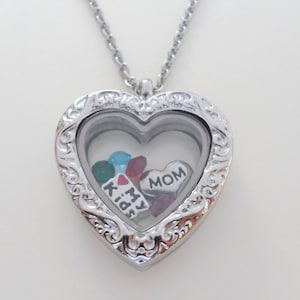 May include: Silver heart-shaped locket necklace with a clear glass insert. The locket contains small charms with the words "MOM", "I", "My", "Kids", and a red heart.