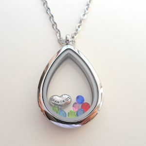 May include: Silver teardrop-shaped locket necklace with a clear glass insert. The locket contains a small heart charm with the inscription "Grandkids" and colorful rhinestones.