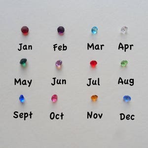 May include: A chart with twelve colored gemstones representing the months of the year. January is red, February is purple, March is blue, April is clear, May is green, June is pink, July is red, August is green, September is blue, October is pink, November is orange, and December is blue.