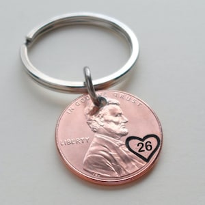 May include: A copper penny keychain with a silver key ring. The penny features an image of Abraham Lincoln and the word "LIBERTY". A black heart with the number "26" is stamped on the penny.