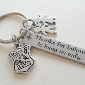 May include: Silver keychain with a police badge charm, a charm of two children holding hands, and a tag that reads "Thanks for helping to keep us safe."