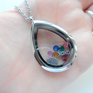 May include: A silver teardrop-shaped locket necklace with a clear glass insert. The locket contains colorful rhinestones and a small charm that reads "I love my Grand Kids". The locket also has the letters "XOXO" inside.